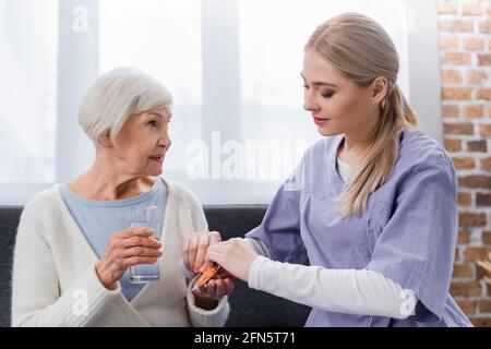 Junge Krankenschwester, die einer älteren Frau mit einem Glas Pillen gibt Wasser Stockfoto