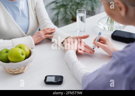 Teilansicht einer Krankenschwester, die bei einer älteren diabetischen Frau in der Nähe des Glukosimeters eine Insulinininspritzung vornimmt, verschwommener Vordergrund Stockfoto