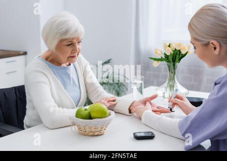 Junge Krankenschwester, die bei einer älteren diabetischen Frau Insulinininspritzung macht Zu Hause Stockfoto
