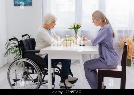 Seitenansicht der Krankenschwester, die einem behinderten Senioren eine Insulinininspritze verabreicht Frau im Rollstuhl Stockfoto