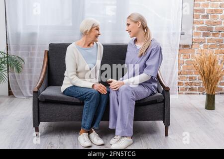 Junge Sozialarbeiterin und ältere Frau lächeln beim Gespräch Sofa zu Hause Stockfoto