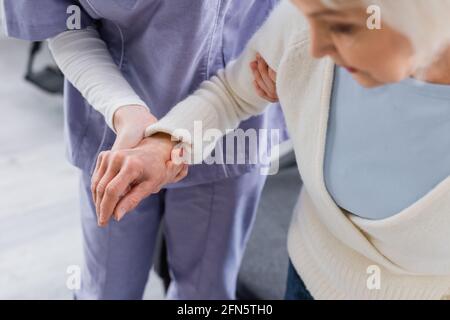 Teilansicht der Krankenschwester, die eine ältere Frau unterstützt, verschwommener Vordergrund Stockfoto