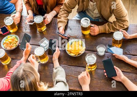 Eine Gruppe von multirassischen Freunden, die ein Bier in einer Bar genießen Restaurant.Junge Menschen Hände halten ein Bier und Smartphone jubeln.Freundschaft und Jugendleben Stockfoto