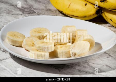 Ein paar Bananen und eine in Scheiben geschnittene Banane auf einem Teller auf einem Tisch. Stockfoto