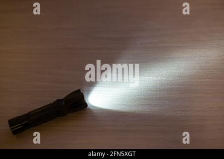 Licht von einer kleinen, Hand gehaltenen schwarzen Taschenlampe auf einer hölzernen Oberfläche, Platz für Kopierraum Stockfoto