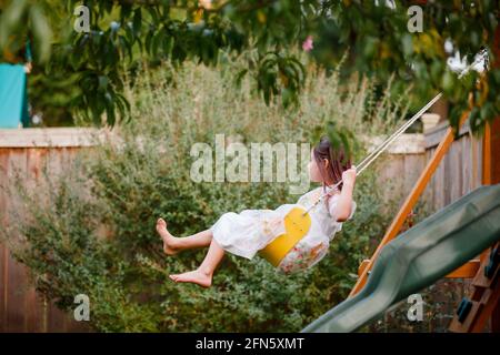 Ein glückliches barfuss Mädchen schwingt auf einem Spielchen unter einem Baum im Sommer Stockfoto