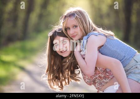 Zwei glückliche schöne junge Teenager-Mädchen auf sonnigen baumgebeulten Landstraße. Stockfoto