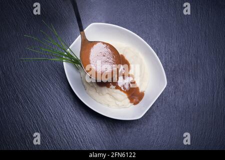 Kartoffelpüree mit Soße auf blackstone-Hintergrund. Dunkles Essen Stockfoto
