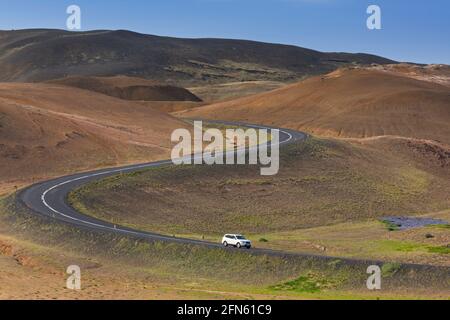 Weißes Auto auf der Route 1 / Ring Road, kurvenreiche Nationalstraße im Sommer am Mount Namafjall / Namaskard, Nordurland Eystra, nordöstlich von Island Stockfoto