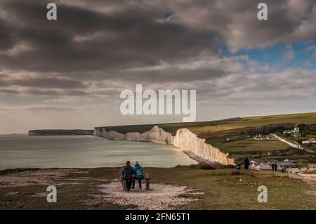 Birling Gap, Eastbourne, East Sussex, Großbritannien. April 2021. Paar auf der Bank, die die herrliche Landschaft genießen. Zusammen unter dunklerem Himmel. David Burr/A Stockfoto