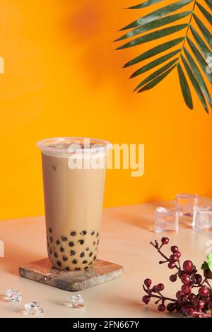 Plastikbecher gefüllt mit frischem und leckerem Bubble Milk Tee Auf einer hölzernen Achterbahn auf dem Tisch Stockfoto