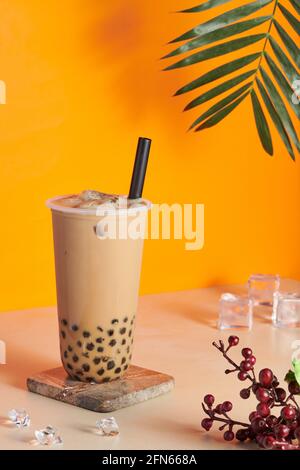 Plastikbecher gefüllt mit frischem und leckerem Bubble Milk Tee Auf einer hölzernen Achterbahn auf dem Tisch Stockfoto