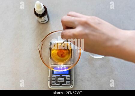 Eine Frau aus Seifenherstellung wiegt aromatische Öle für die Herstellung von Kosmetika im Küchenmaßstab. Spa im Haus. Kleinunternehmen. Stockfoto