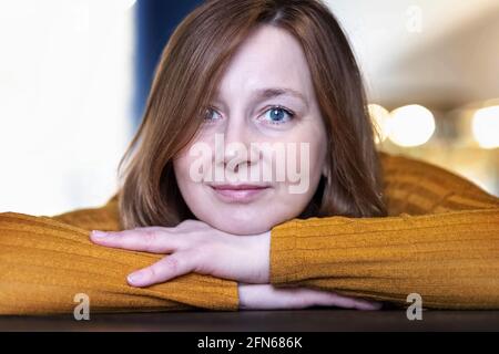 Porträt einer lächelnden Frau mit dem Kopf in den Händen auf dem Tisch. Stockfoto