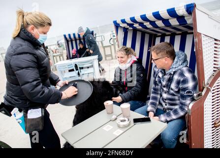 Norderney, Deutschland. Mai 2021. Die Kellnerin Nina (l.) bedient Anet und Christoph aus der Nähe von Oldenburg, die mit ihrem Hund Murphy in einer Strandliege vor dem Surfcafe an der Strandpromenade sitzen. In Niedersachsen dürfen Hotels, Ferienwohnungen und andere Unterkünfte in Regionen mit einer siebentägigen Inzidenz von weniger als 100 Tagen wieder Gäste empfangen. Quelle: Hauke-Christian Dittrich/dpa/Alamy Live News Stockfoto