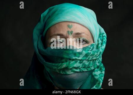 Eine Frau mittleren Alters mit fast vollständig verdecktem Gesicht Ein grüner Schal hat zwei Herzen auf ihre Stirn gezogen Stockfoto