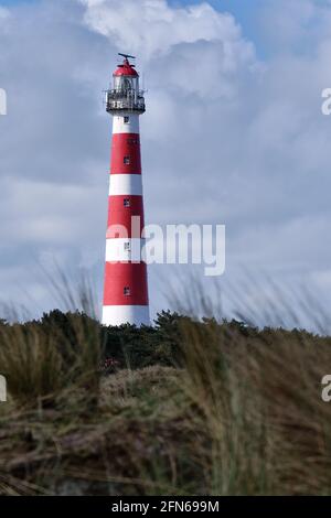 Klassischer, historischer, alter rot-weißer Leuchtturm mit Dünen und Gras, sonniger windiger Tag und turbulente Wolken auf der niederländischen Insel Ameland, Hollum Stockfoto