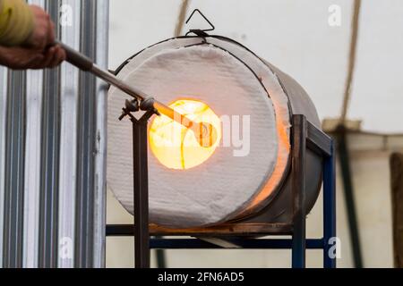 Ein Glasgebläse verwendet einen Glory-Loch-Gasofen, um das Glas auf dem Blasrohr / Blasrohr / Blasrohr zu erhitzen und es geschmolzen zu halten, bevor er bläst & formt. VEREINIGTES KÖNIGREICH Stockfoto