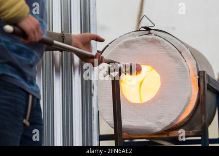 Ein Glasgebläse verwendet einen Glory-Loch-Gasofen, um das Glas auf dem Blasrohr / Blasrohr / Blasrohr zu erhitzen und es geschmolzen zu halten, bevor er bläst & formt. VEREINIGTES KÖNIGREICH Stockfoto