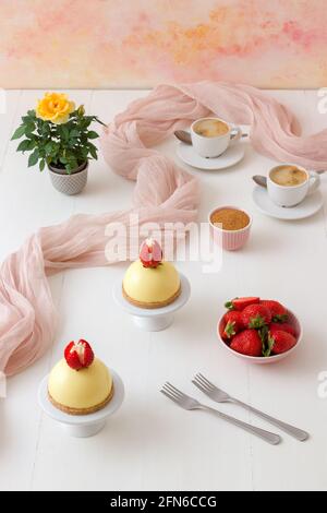 Hausgemachte Zitrone No-Bake Käsekuchen Kuppel mit frischen Erdbeeren. Weißer Holztisch mit gelben Rosées im Hintergrund. Stockfoto