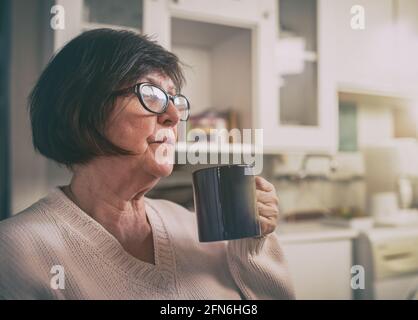 Ältere Frau ruht sich aus und trinkt heißen Kaffee in der Tasse Küche zu Hause Stockfoto