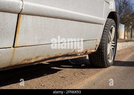 Metallkorrosion über dem Rad des alten weißen Autos. Rostige unordentliche Oberfläche. Beschädigte Grunge schmutzige Textur von Straßensalz. Rosthintergrund. Schützen des Stockfoto