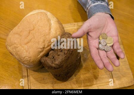 Letztes Geld, um Brot zu kaufen. Ein Laib Brot und die Hand eines alten Mannes. Es gibt einige Münzen in der Handfläche. Stockfoto