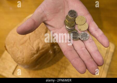 Letztes Geld, um Brot zu kaufen. Ein Laib Brot und die Hand eines alten Mannes. Es gibt einige Münzen in der Handfläche. Stockfoto