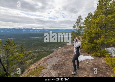 Frau in weißer Jacke, schwarze Hose, die am Rande eines Wanderweges auf einem Berg steht und Fotos macht, um die landschaftliche Aussicht in Yukon zu fotografieren. Stockfoto