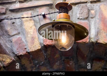 Laterne aus Eisen im Retro-Stil mit Glasschirm auf dem Mauerwerk-Bogen mit edison-Lampe, dekoratives architektonisches Element in der Nähe des alten Stils. Stockfoto