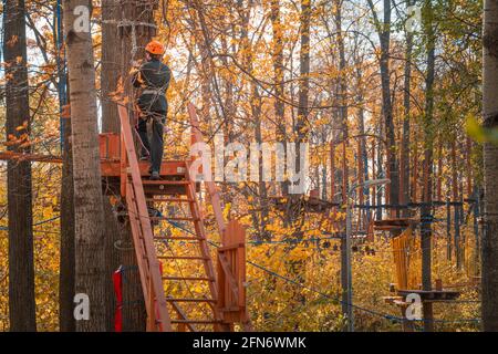 Kazan, Russland - 03. Oktober 2020: Ein junger Mann in einem Helm klettert in einem Seilpark eine Leiter zu einem Baum. Stockfoto