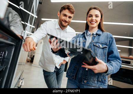 Junges Paar, das sich für einen neuen Elektroofen im Hypermarkt entscheidet Stockfoto
