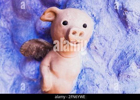 Geflügeltes Schwein aus Lehm und bemalt auf einer blauen Himmel Hintergrundwand. Stockfoto