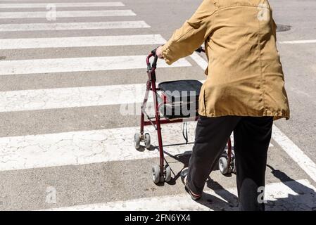 Eine alte Frau überquert einen Fußgängerübergang mit Hilfe eines Rollator-Walkers. Stockfoto