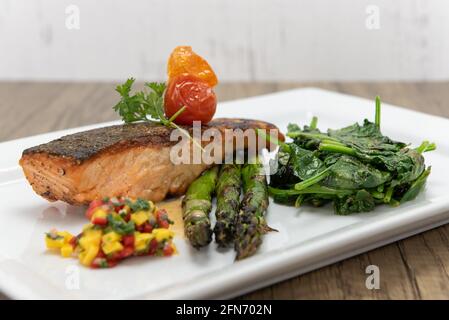 Gegrilltes Lachssteak, serviert mit Spargel und Spinat, um dem Appetit auf Meeresfrüchte zu frönen. Stockfoto