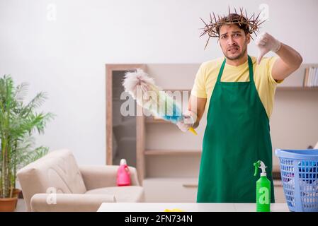 Junger männlicher Auftragnehmer, der auf dem Kopf einen stacheligen Kranz trägt und Hausarbeit leistet Stockfoto