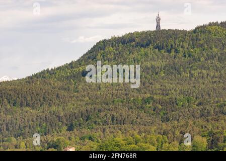 Fernsehturm auf dem Berg. Grüner Frühlingswald in den Bergen Österreichs. Auf dem höchsten Hügel gibt es einen Turm in einem schönen Design. Stockfoto