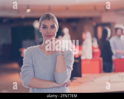 Schöne blonde Geschäftsfrau Blick auf die Kamera und lächelnde Mitarbeiter vielfältig Team im modernen Open Space Büro im Hintergrund Stockfoto