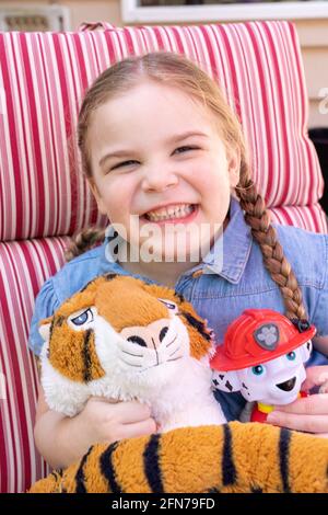 Lynwood, Washington, USA. Vierjähriges Mädchen, das Spaß mit ihrem gefüllten Feuerwehrhund und Tiger hat. (MR) Stockfoto