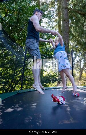 Lynwood, Washington, USA. Das vierjährige Mädchen und ihr Vater hüpfen auf einem Trampolin in ihrem Hinterhof. Stockfoto