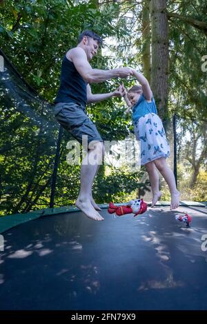 Lynwood, Washington, USA. Das vierjährige Mädchen und ihr Vater hüpfen auf einem Trampolin in ihrem Hinterhof. Stockfoto