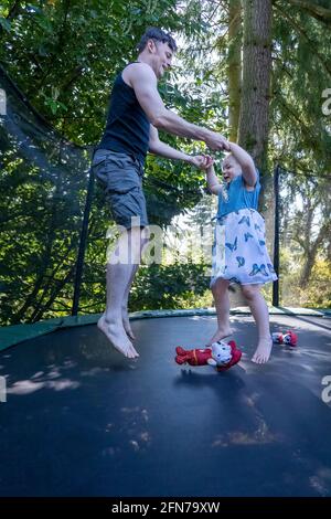 Lynwood, Washington, USA. Das vierjährige Mädchen und ihr Vater hüpfen auf einem Trampolin in ihrem Hinterhof. Stockfoto