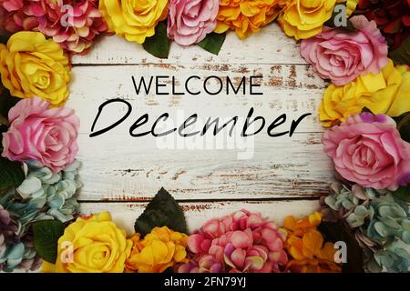 Begrüßungstext für Dezember mit Blumenrand auf hölzernem Hintergrund Stockfoto