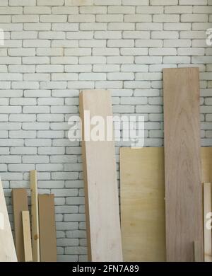 Die Holzplanken verschiedener Größen stützen sich auf die weiße Ziegelwand. Morgendliche Arbeitsatmosphäre im Werkstattraum. Stockfoto