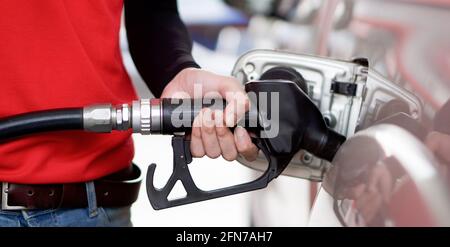 Tankstellenmitarbeiter in roter Uniform füllen Bronze Pickup LKW-Tank. Nahaufnahme Hand mit schwarzer Gaspumpendüse. Stockfoto