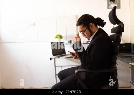 Hispanischer junger Mann in einem schwarzen Anzug, der im Heimbüro ist An seinem Schreibtisch machte er sich große Sorgen um die Arbeit Stockfoto