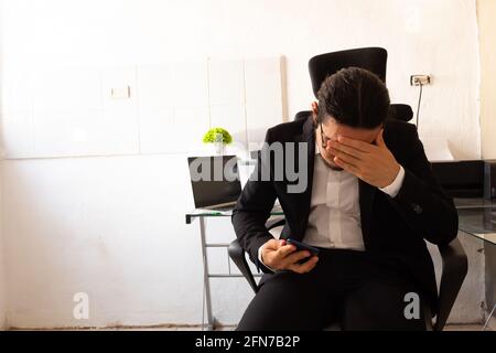 Hispanischer junger Mann in einem schwarzen Anzug, der im Heimbüro ist An seinem Schreibtisch machte er sich große Sorgen um die Arbeit Stockfoto