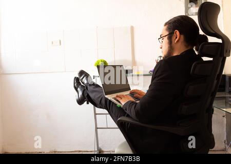Hispanischer junger Mann in einem schwarzen Anzug, der im Heimbüro ist Sehr komfortabel und entspannt Stockfoto