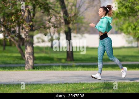 Foto in voller Länge von einer Frau, die am frühen Morgen im Park läuft. Attraktiv aussehende Frau, die sich fit und gesund hält. Gesundes Lifestyle-Konzept. Stockfoto