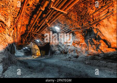 Tunnel des Bergbaus einer unterirdischen Mine. Viele Rohrleitungen an der Decke und Schienenbahn für Trolleys Stockfoto